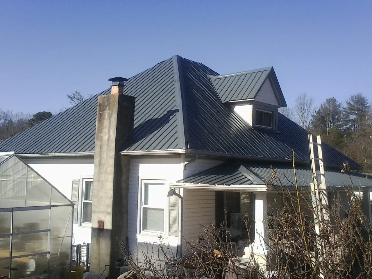 Dark blue standing seam metal roof on a white farmhouse with dormer — Slate & Tile Roof Repair by Roofing Brothers in Barnum