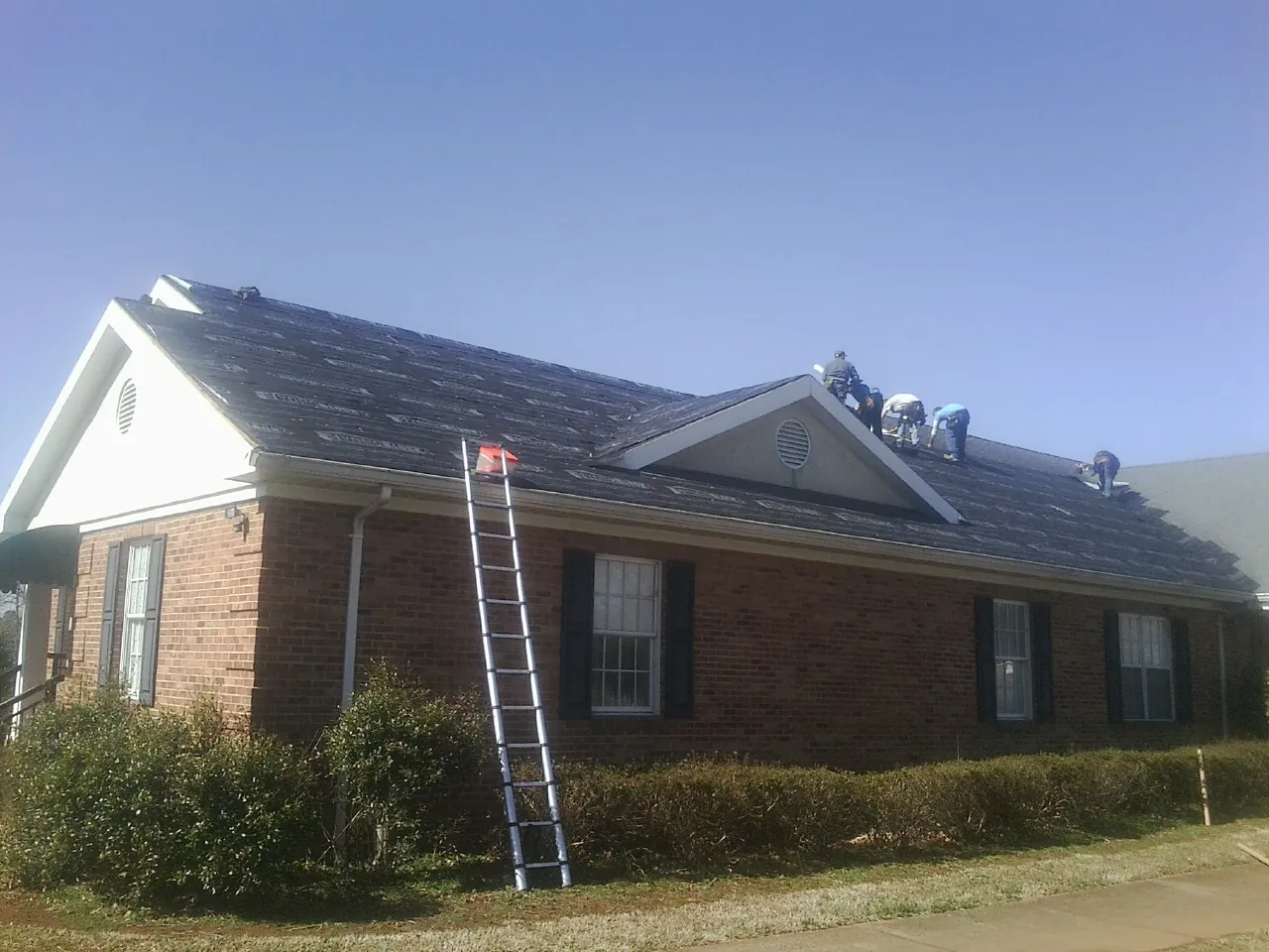 Crew tearing shingles off a brick ranch roof with a ladder set — Metal Roof Repair work by our crew in Barnum