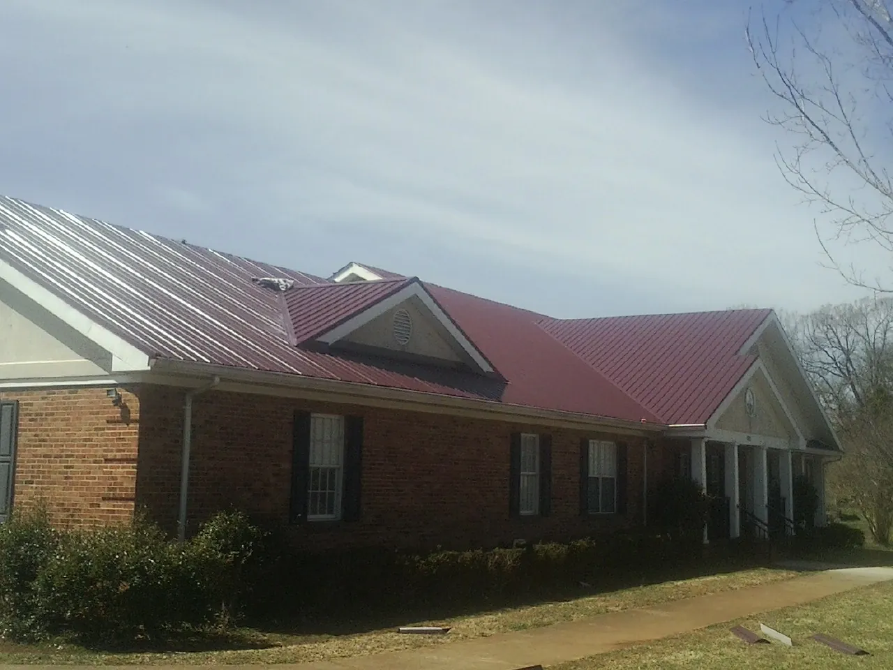Red metal roof with gabled entries on a long brick building, from a Hail Damage Roof Repair job in Barnum