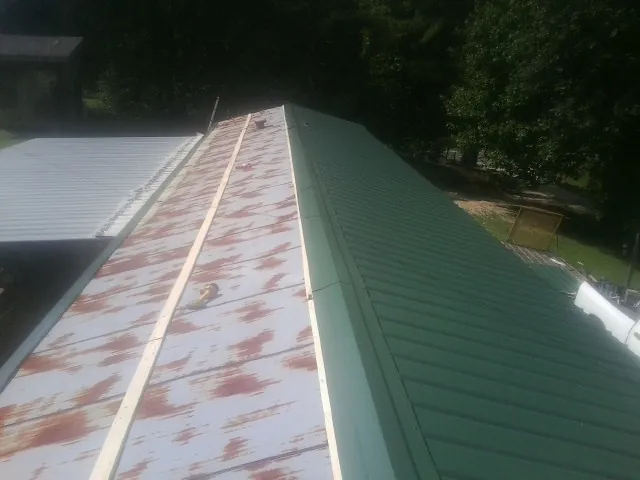 Old rusted panels beside newly installed green metal roofing — Wind Damage Roof Repair by Roofing Brothers in Barnum