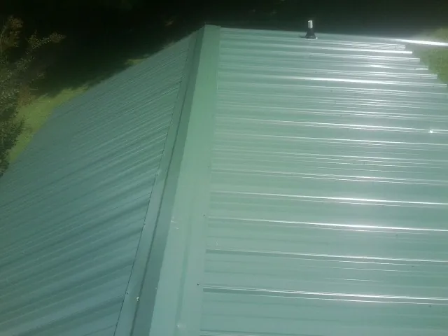 New green metal panels meeting at the ridge of a roof — Flat Roof Repair work by our crew in Barnum