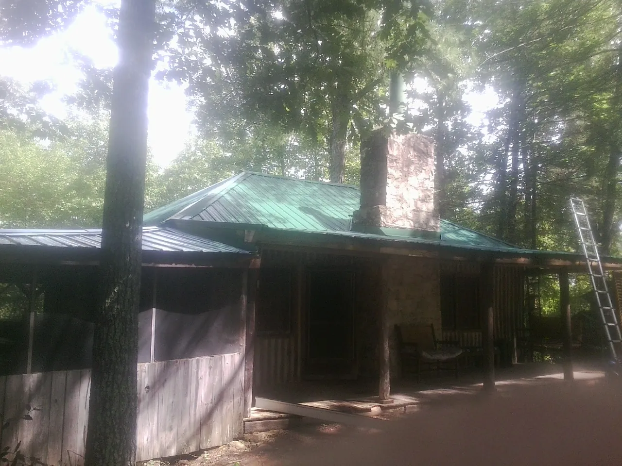 Green metal roof and stone chimney above a log cabin porch in Barnum