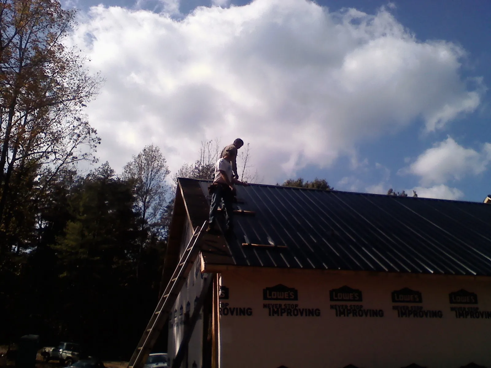 Roofer fastening dark metal panels high against a cloudy sky, from a Roof Inspection job in Barnum