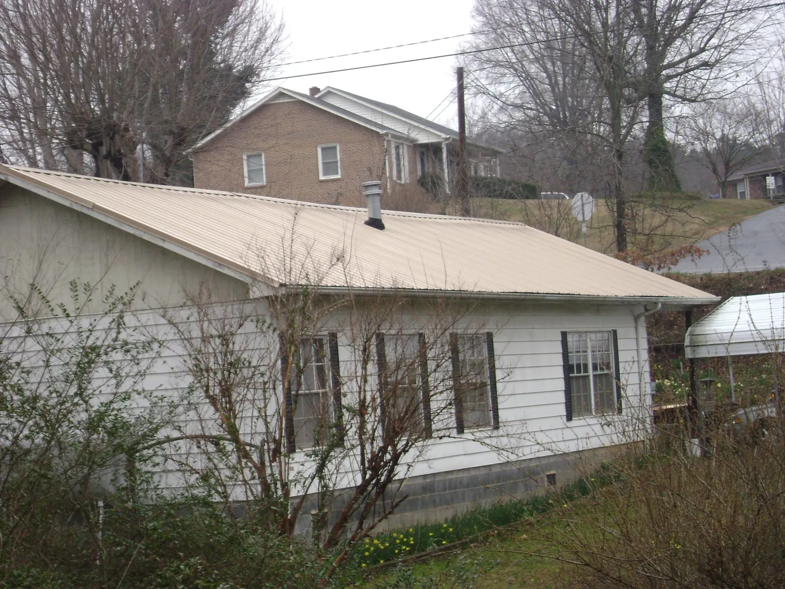 Tan metal roof on a white sided house set into a hillside — Commercial Roofing by Roofing Brothers in Barnum