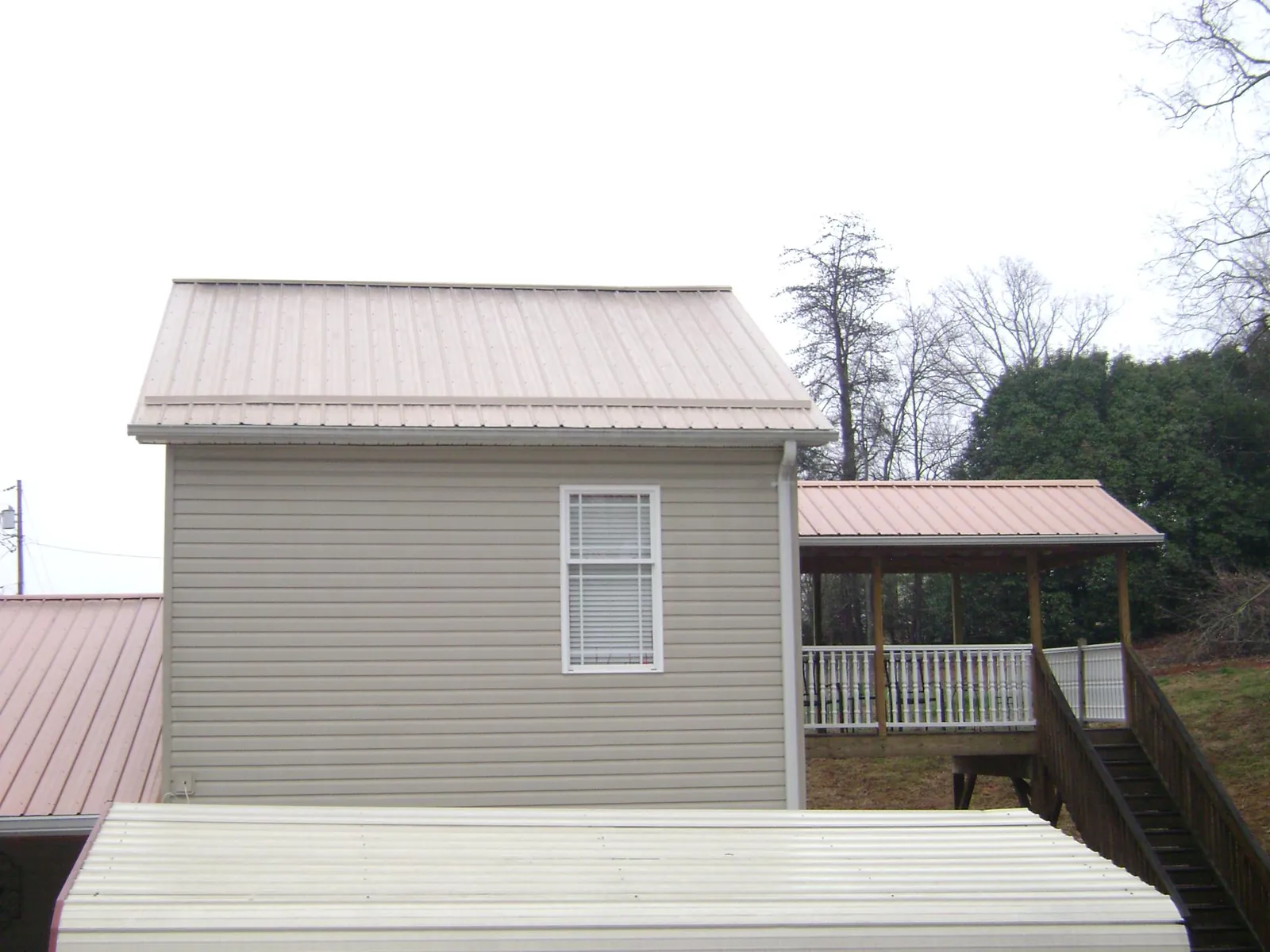 Tan metal roofs on a two story addition and attached porch, from a Roof Replacement job in Barnum